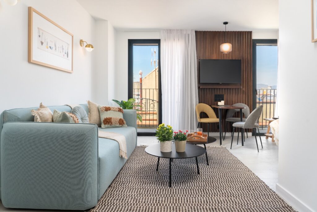 Open-plan studio with soft-toned furnishings, textured rug, and private balcony access through large glass doors.