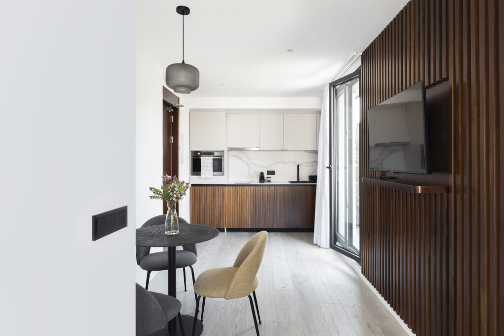 Modern open-plan kitchen and dining space at master La Rambla Barcelona featuring wood finishes, marble backsplash, and flat-screen TV.