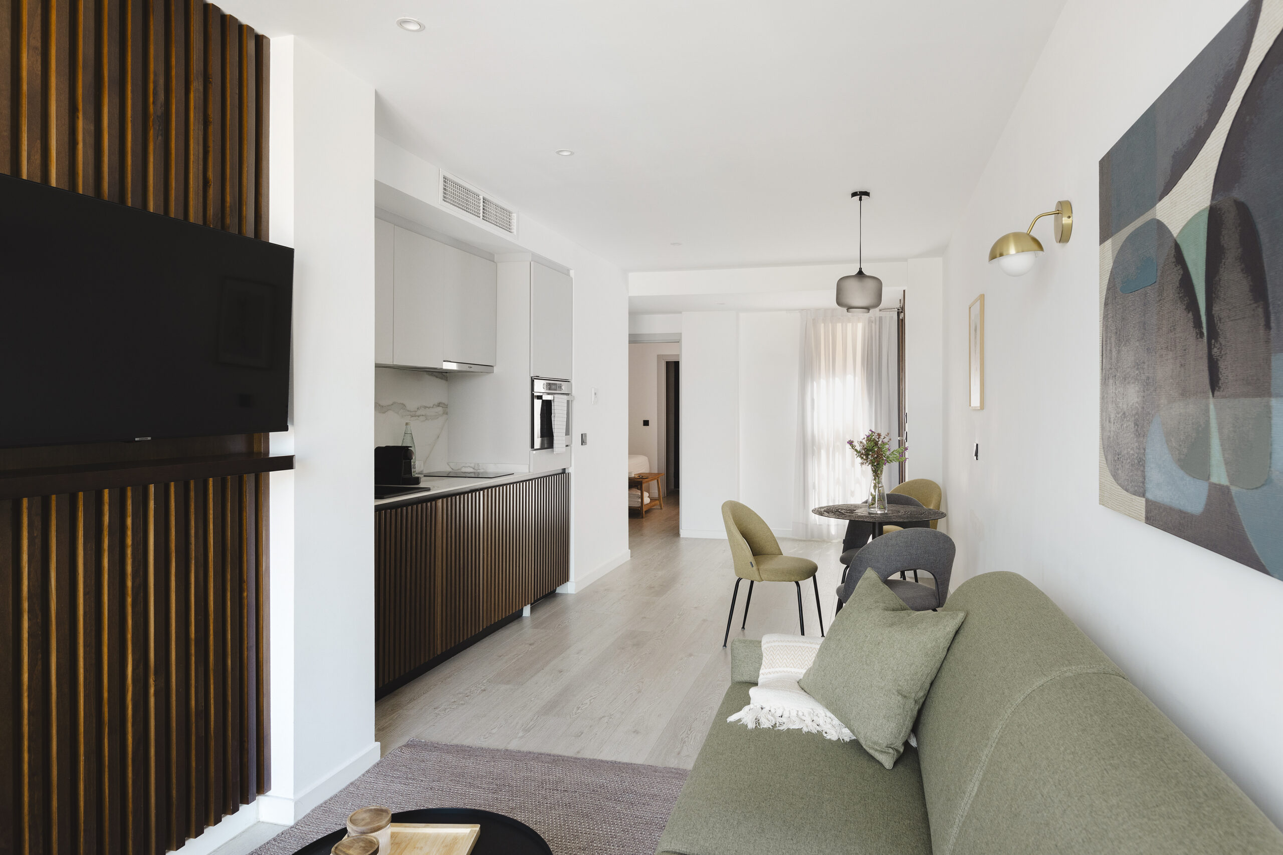 Modern open-plan living area at master La Rambla Barcelona with green sofa, flat-screen TV, and sleek kitchen design.