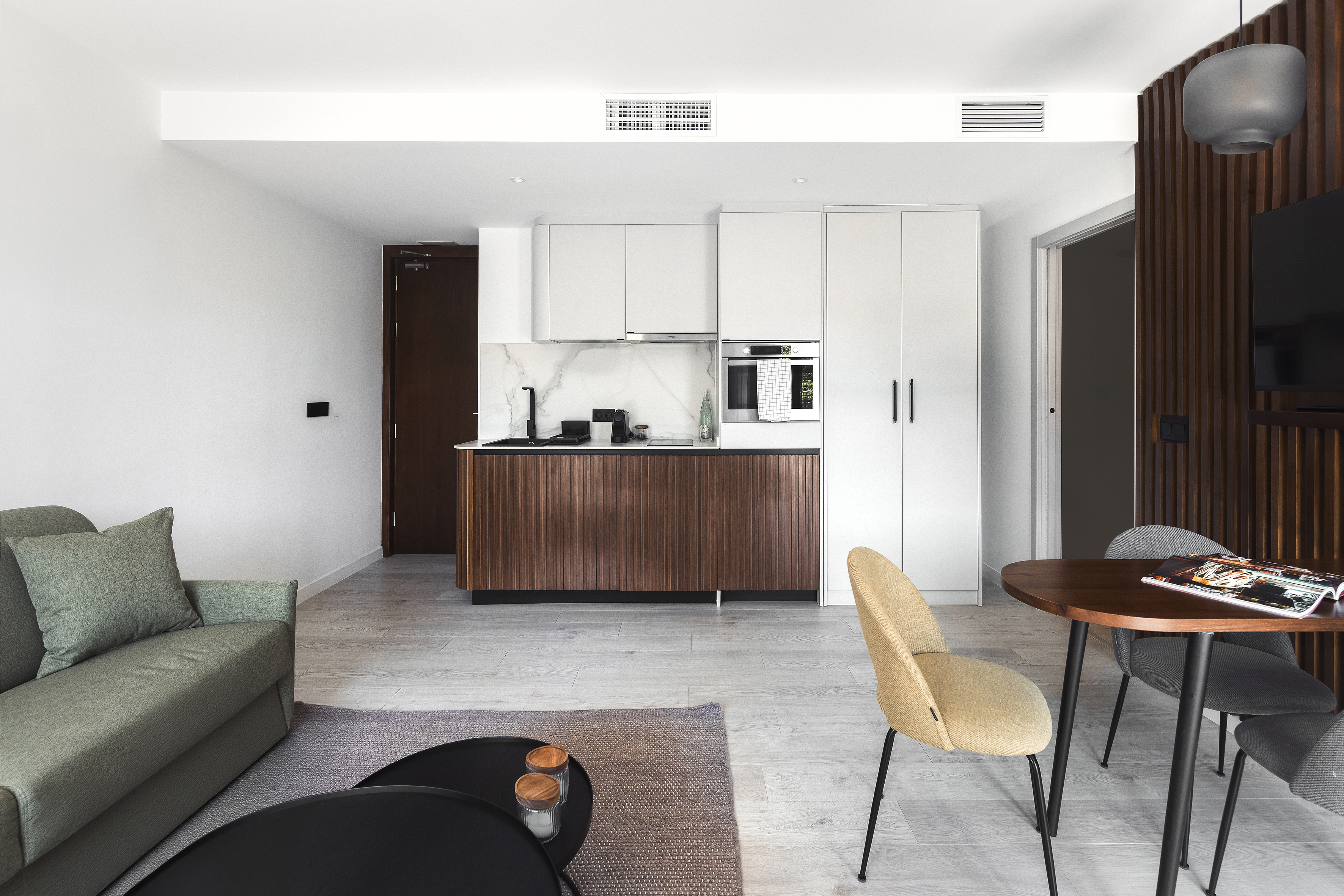 Open-plan kitchen and living area at master La Rambla Barcelona with wood finishes, sofa, dining table, and flat-screen TV.