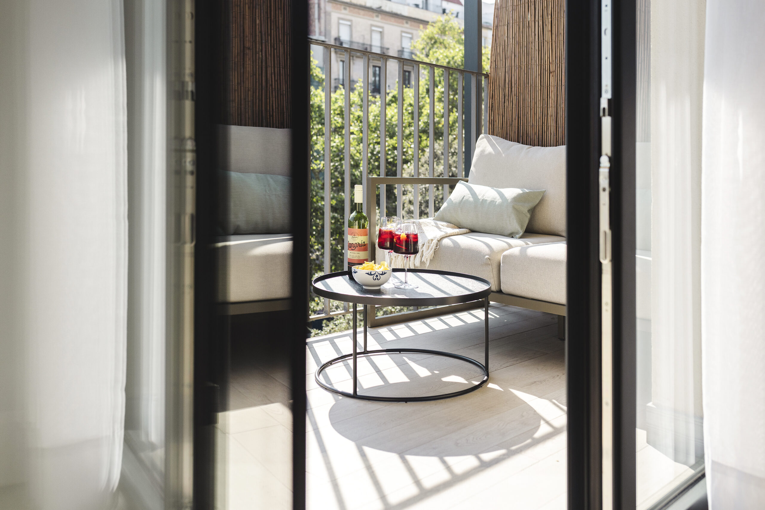 Private balcony at master La Rambla Barcelona with a cozy lounge sofa, round table, and sangria glasses overlooking the city.