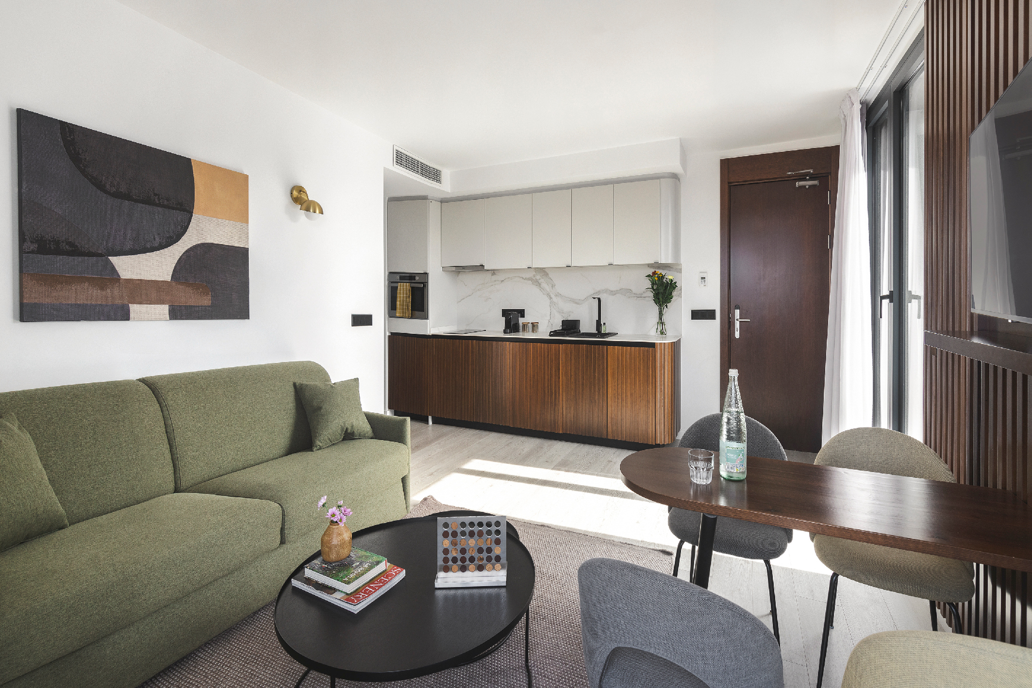 Contemporary penthouse living room with green sofa, wood accents, and full kitchen, opening onto a private terrace.