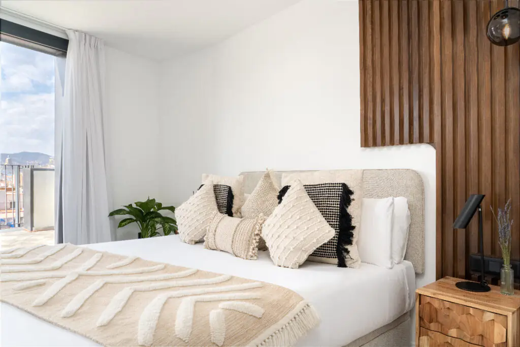 Elegant bedroom with decorative pillows, wooden accent wall, and glass doors leading to the private terrace.