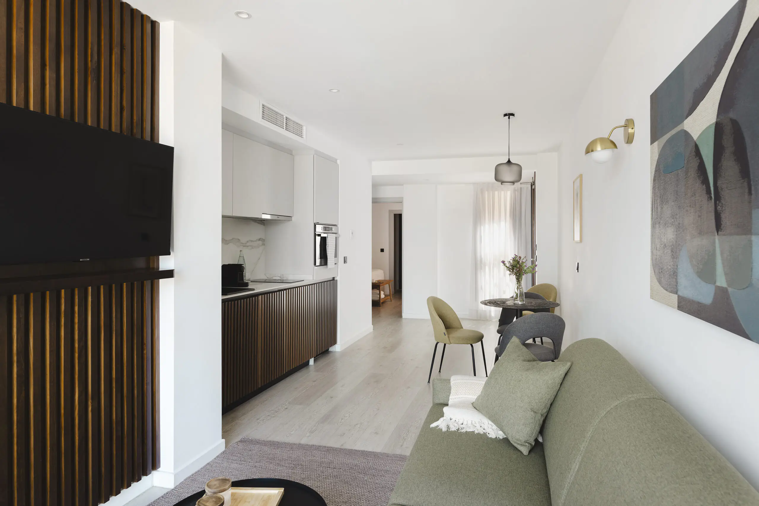 Modern open-plan living area at master La Rambla Barcelona with green sofa, flat-screen TV, and sleek kitchen design.