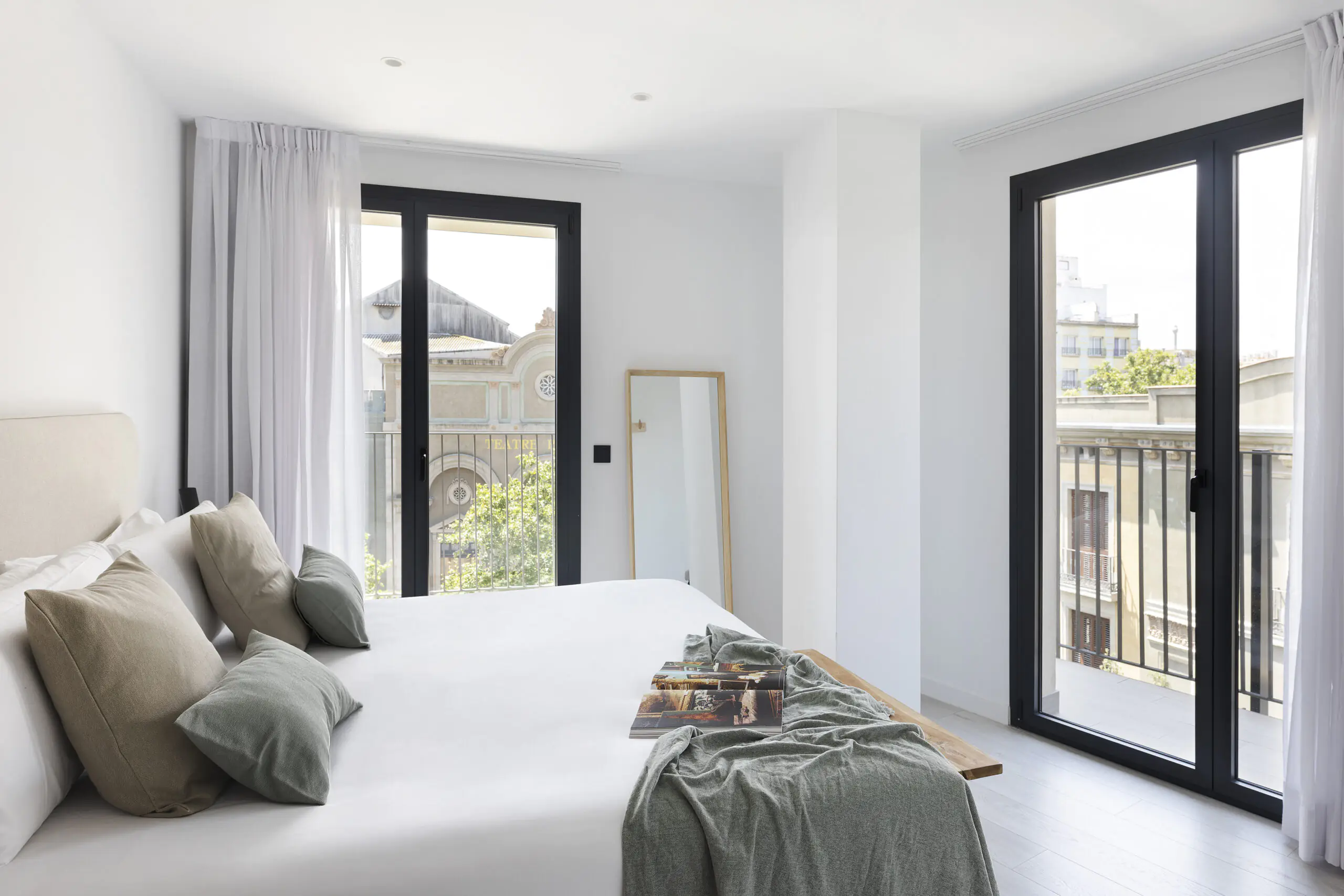 Spacious bedroom at master La Rambla Barcelona with double bed, soft neutral décor, large windows, and views of Barcelona’s architecture.